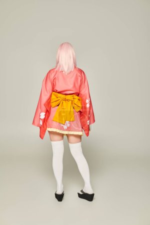 back view of anime style woman in blonde wig and short pink kimono with white knee socks on grey