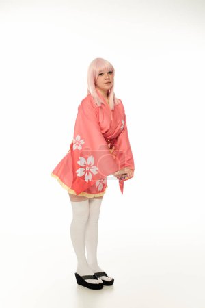 full length of young model with blonde hair posing in pink kimono and white knee socks on white
