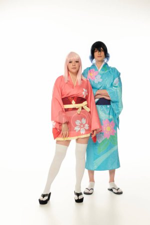 Anime-Stil Paar in lebendiger traditioneller Kleidung und Perücken blickt in die Kamera auf weiß, volle Länge