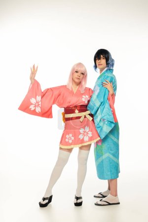 junge Frau im Kimono winkt neben einem Mann im Anime-Stil mit Perücke auf weißer, asiatischer Subkultur-Mode