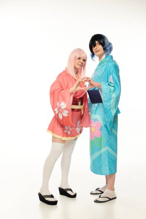 glückliche junge Cosplayer in bunten Kimonos, die Herzzeichen mit Händen auf weißem Anime-Stil zeigen