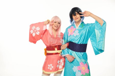 vibrant anime style couple in kimonos showing victory gesture and looking at camera on white