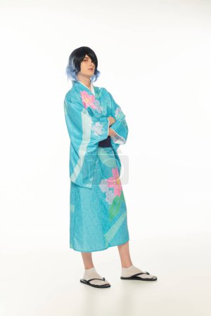 longitud completa de hombre joven en colorido kimono y peluca posando con brazos cruzados en blanco, cosplayer