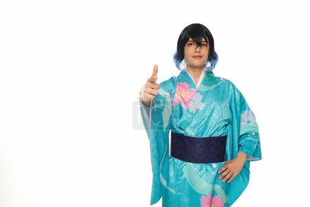 young creative man in blue kimono and wig pointing with finger at camera on white, cosplay culture