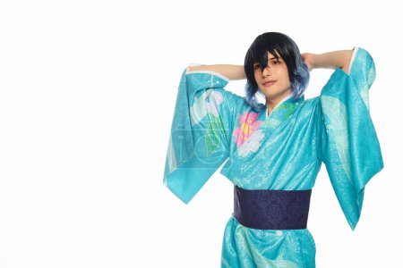 junger Mann im blauen Kimono mit den Händen hinter dem Kopf, der in die Kamera auf weißem, verträumtem Cosplayer blickt