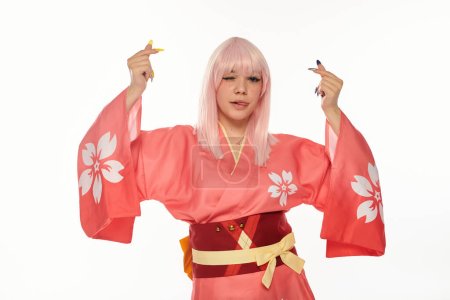 verspielte blonde Frau in buntem Kimono, die Zunge herausstreckt und Mini-Herzen auf weißem Grund zeigt