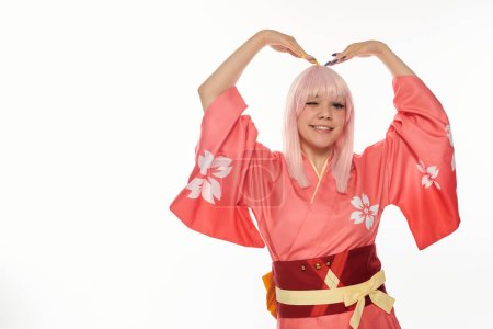 coqueta mujer de anime en kimono rosa de pie en pose expresiva y guiño sobre fondo blanco