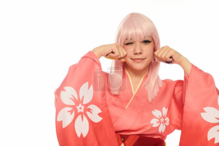 mujer anime en kimono rosa y peluca rubia sosteniendo puños cerca de la cara y guiñando el ojo a la cámara en blanco