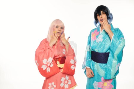 asombrada pareja de anime en coloridos kimonos y pelucas tocando caras en blanco, tendencia cosplay