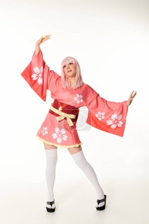 young expressive woman in pink kimono and blonde wig posing with outstretched hands on white
