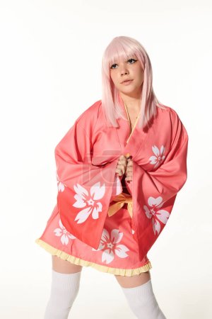 attraktive Frau im Anime-Stil mit blonder Perücke und rosa Kimono im Stehen und Wegschauen auf Weiß
