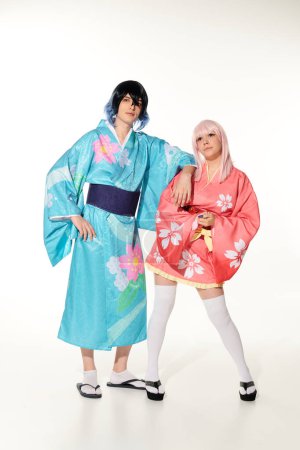 pleine longueur de jeune et dynamique couple en kimonos et perruques sur blanc, asiatique cosplay sous-culture