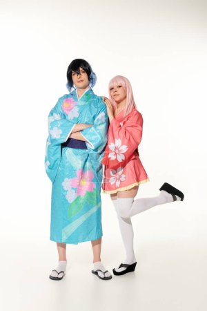 Frau stützt sich auf Freund in buntem Kimono und Perücke stehend mit verschränkten Armen auf Weiß, Cosplay