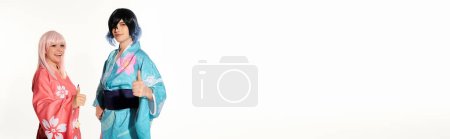 Téléchargez les photos : Cosplayers souriants en kimonos et perruques montrant pouces vers le haut et regardant la caméra sur blanc, bannière - en image libre de droit