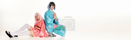 Mann im Kimono mit betenden Händen neben Anime-Frau mit blonder Perücke sitzt auf weißem, waagerechtem Banner