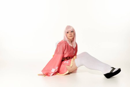 femme rêveuse en kimono rose et perruque blonde assis et regardant loin sur blanc, anime personnage