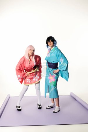 young playful cosplayers in kimonos and wigs with hands on hips on purple carpet in white studio