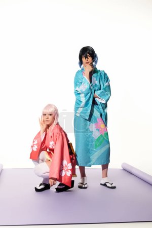 Blonde Anime-Frau sitzt neben Mann im Kimono und Perücke auf lila Teppich im weißen Studio
