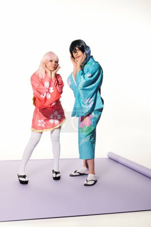 Verspieltes Paar Cosplayer in lebendigem Outfit, die Gesichter auf lila Teppich und weißem Hintergrund berühren