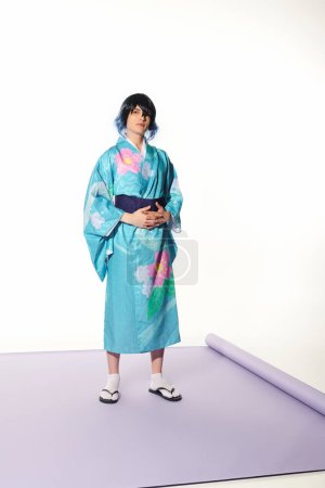 pleine longueur de jeune homme en kimono bleu et perruque sur tapis violet en studio blanc, concept cosplay