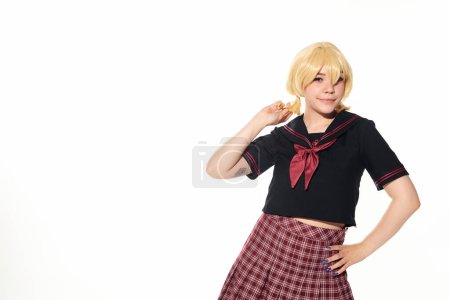 Foto de Sonriente anime estilo mujer en uniforme escolar de la mano en la cadera y mirando a la cámara en blanco - Imagen libre de derechos