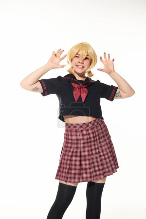 funny cosplay woman in yellow blonde wig and school uniform showing scaring gesture on white