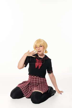 stylish blonde woman in school uniform showing blonde wig while sitting on white, anime character