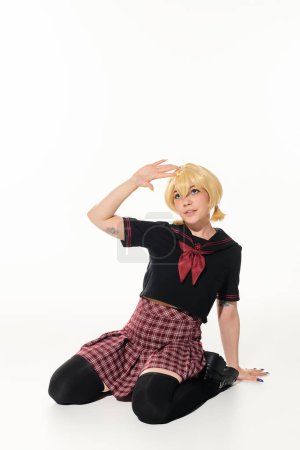 tattooed blonde woman in stylish school uniform sitting and waving hand on white, anime style