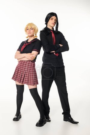 full length of young cosplayers in school uniform and wigs posing with folded arms on white