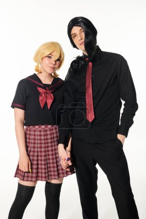 young models in wigs and school uniform holding hands and looking at camera on white, cosplayers