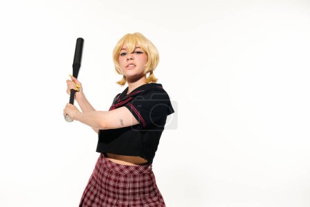 femme irritée en uniforme scolaire et perruque debout avec batte de baseball sur blanc, personnage cosplay