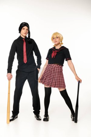 pareja de cosplayers en uniforme escolar y pelucas con bates de béisbol en blanco, longitud completa