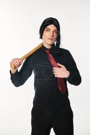 trendy cosplayer in black clothes and wig touching red tie and holding baseball bat on white