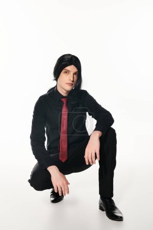 fashionable man in black clothes and  wig with red tie sitting on haunches on white, cosplay trend