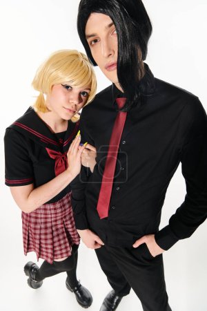wide angle view of cosplay style couple in wigs and dark students uniform looking at camera on white