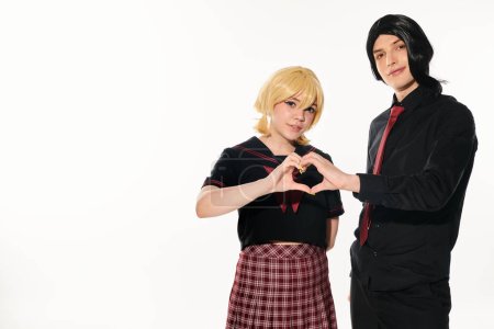pareja cosplay en pelucas negras y rubias mostrando el signo del corazón con las manos mirando a la cámara en blanco