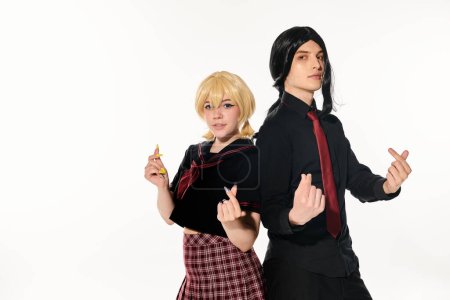 Foto de Jóvenes estudiantes de estilo anime en uniforme oscuro y pelucas que muestran mini corazones con los dedos en blanco - Imagen libre de derechos