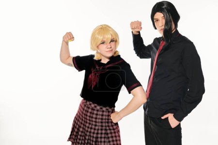 Photo for Expressive students in dark uniform and wigs showing muscles and looking at camera on white - Royalty Free Image