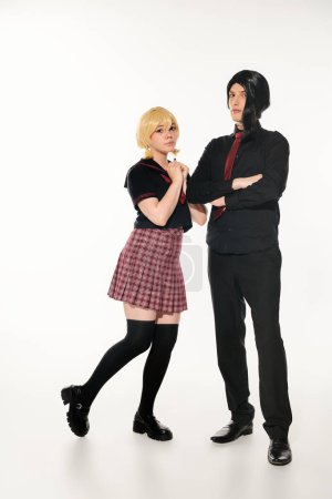 woman in blonde wig near confident man in black clothes with folded arms on black, cosplay students