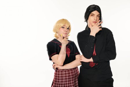 serious students in dark uniform with hands near faces looking at camera on white, trendy cosplayers