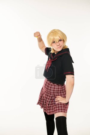 angry woman in school uniform and yellow blonde wig showing fist on white, cosplay character