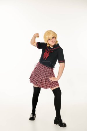 aggressive anime style woman in school uniform and yellow blonde wig showing fist on white