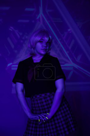 junge blonde Frau in Schuluniform in Neonlicht vor blauem abstrakten Hintergrund, Cosplay-Charakter