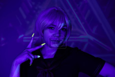 mujer de estilo anime con peluca rubia y manicura fluorescente mostrando signo de victoria en luz de neón azul