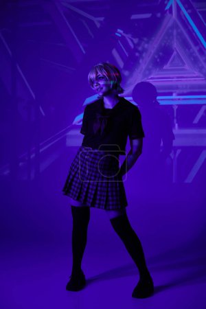 volle Länge der Frau in Schuluniform in blauem Neonlicht auf abstraktem Hintergrund, Anime-Konzept