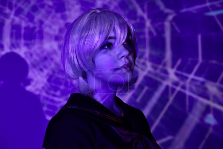Photo for Portrait of young anime style woman in blonde wig in blue neon light on abstract backdrop, cosplay - Royalty Free Image