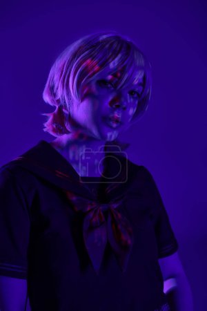 Porträt einer jungen Frau mit blonder Perücke, die in blauem Neonlicht in die Kamera blickt, Cosplay-Kulturkonzept