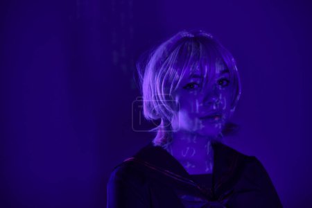 portrait of charming female cosplayer in blonde wig with hieroglyphs projection in blue neon light