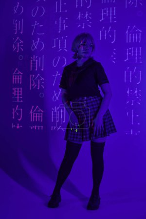 junge Frau in Schuluniform in blauem Neonlicht mit Hieroglyphen-Projektion, Cosplay-Konzept