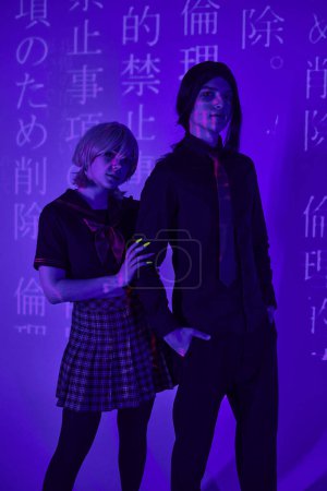 young cosplayers in students uniform and wigs posing in blue neon light with hieroglyphs projection
